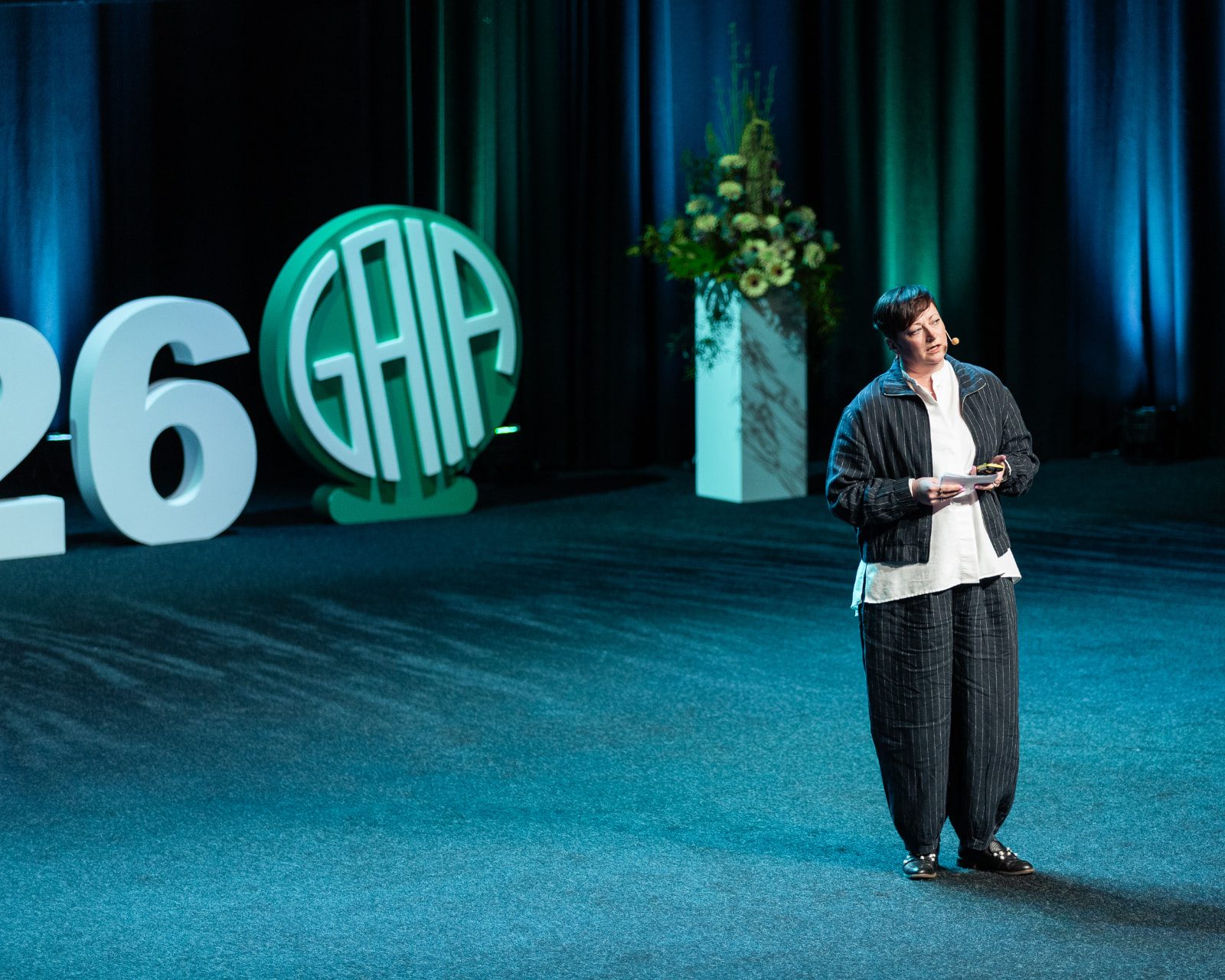 A speaker stands on the GAIA Conference stage, with the GAIA logo and stage letters behind her.